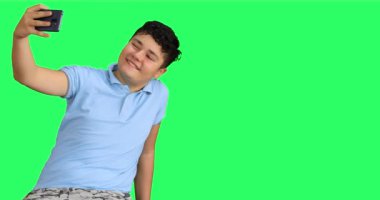 Yeşil arka planı olan yakışıklı genç bir çocuk selfie çekiyor ve kameraya başparmaklarını gösteriyor.