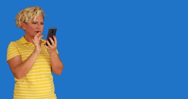 一个中年妇女的画像 带着手机 被蓝屏彩色的关键背景惊呆了 — 图库视频影像