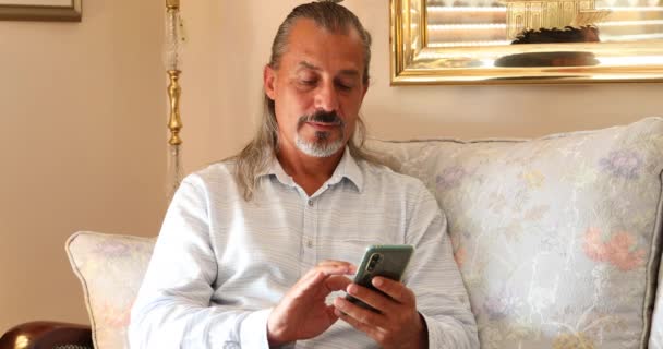 Portrét Hispánského Muže Středního Věku Sedícího Pohovce Používajícího Doma Smartphone — Stock video