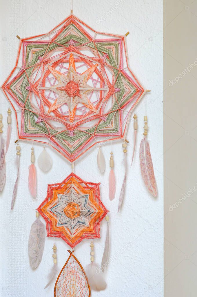 Closeup handcrafted modern dreamcatcher with two mandalas, feathers and wooden beads in details on white wall background