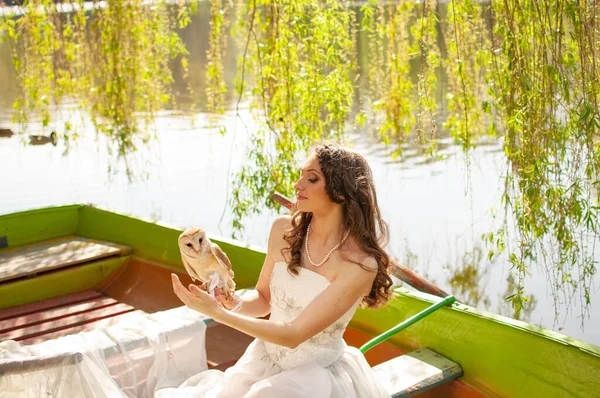 Magic portrait of beautiful bride in white wedding dress with real barn owl on boat