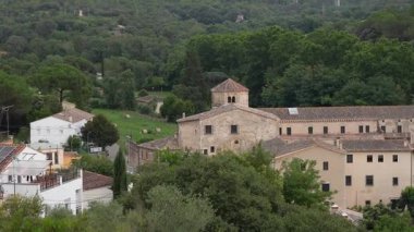 Merkezi çan kulesi olan antik taş manastır ve yoğun yeşil orman, tarlalar ve huzur dolu kırsal bir vadide beyaz cepheli geleneksel köy evleri arasına yerleştirilmiş kırmızı kil kiremitli çatılar.