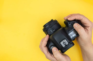 Fotoğrafçının elindeki dijital kamera. Eller sarı arkaplanda dijital kamera ve metin için kopyalama alanı kullanıyor. Üst görünüm, minimalizm.