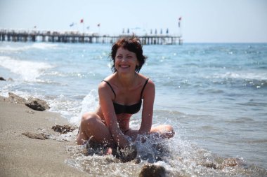 Güzel bir kadın güneşin denizin tadını çıkarma. Sahilde oturan bir genç bayan. Kumsalda güneşlenirken güzel yetişkin kadın. 