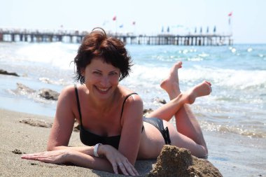 Güzel bir kadın güneşin denizin tadını çıkarma. Sahilde oturan bir genç bayan. Kumsalda güneşlenirken güzel yetişkin kadın. 