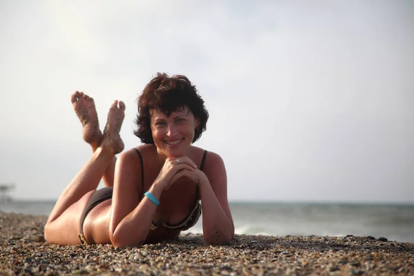 美しい女性が海で日光浴します ビーチに座っている若い女性 ビーチでの日光浴のアダルト美人 — ストック写真