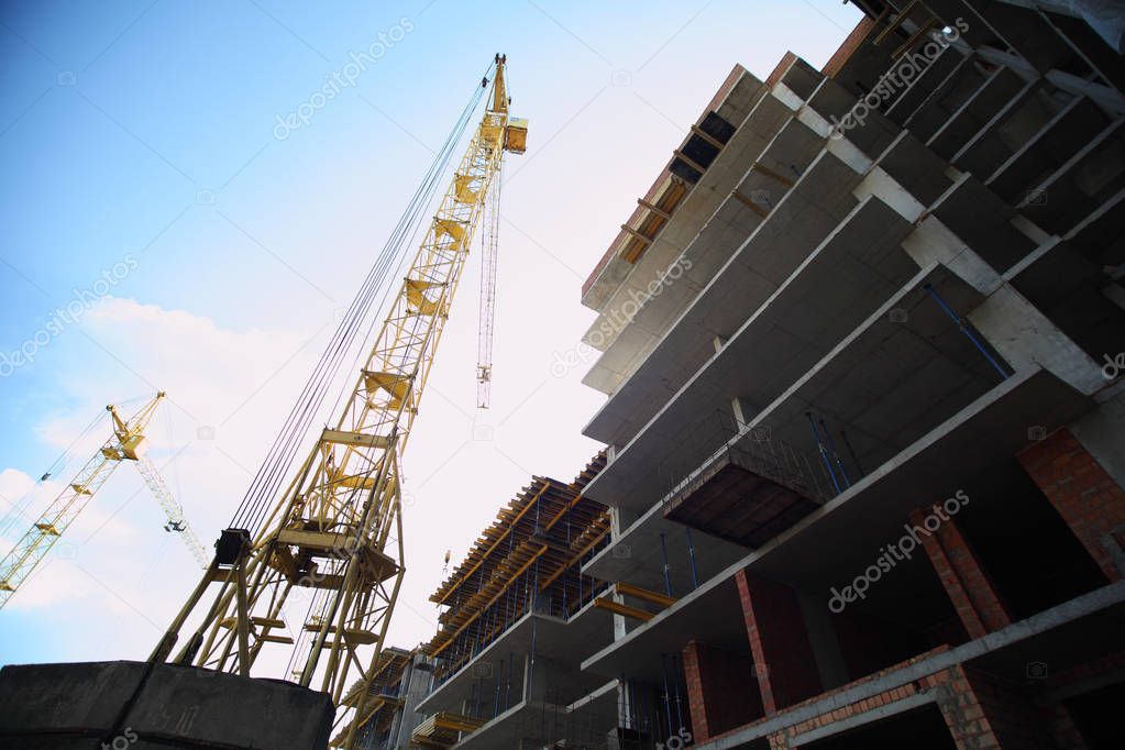 Construction of a residential multi-storey building. New residential area. Working crane on the construction of the house. Construction site with cranes on sky background. 