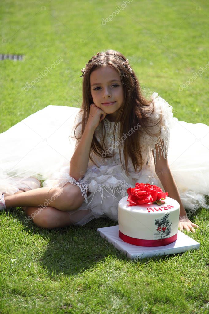 Little Alice is sitting on the grass. Alice and cake.