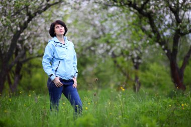 Bahar bahçesinde kamera için poz güzel olgun kadın. Kız elma ağaçlarının çiçekli sahiptir.