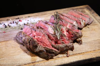 Orta pişmiş biftek, ahşap bir tahtanın üzerinde sos ve baharatlarla dilimlenmiş. Lezzetli biftek. Sebze yastığında az pişmiş biftek. Tahta tabakta biftek.. 