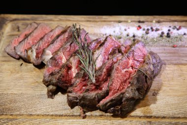 Sebze yastığında az pişmiş biftek. Tahta tabakta biftek. Orta pişmiş biftek, ahşap bir tahtanın üzerinde sos ve baharatlarla dilimlenmiş. Nefis biftek.. 