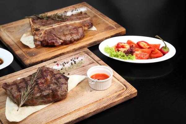 Medium-roasted steak cut into pieces on a wooden board with sauce and seasonings. Delicious steak. Beef steak medium rare on vegetable cushion. Beef steak on wooden plate.
