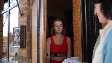 Vinnitsa, Ukrayna - 19 Ekim 2019: Genç, güzel bir kız evinin kapısında bir postacıdan bir paket alır. Müşteri kapısına paket teslimatı. Editör görüntüleri.