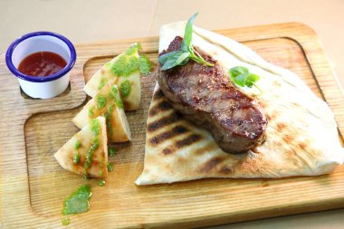 Orta pişmiş biftek, ahşap bir tahtanın üzerinde sos ve baharatlarla dilimlenmiş. Lezzetli biftek. Sebze yastığında az pişmiş biftek. Tahta tabakta biftek..