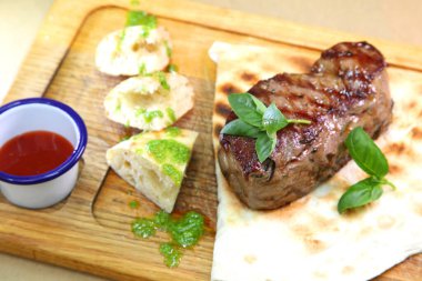 Orta pişmiş biftek, ahşap bir tahtanın üzerinde sos ve baharatlarla dilimlenmiş. Lezzetli biftek. Sebze yastığında az pişmiş biftek. Tahta tabakta biftek..