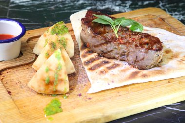 Orta pişmiş biftek, ahşap bir tahtanın üzerinde sos ve baharatlarla dilimlenmiş. Lezzetli biftek. Sebze yastığında az pişmiş biftek. Tahta tabakta biftek..