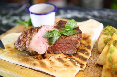 Orta pişmiş biftek, ahşap bir tahtanın üzerinde sos ve baharatlarla dilimlenmiş. Lezzetli biftek. Sebze yastığında az pişmiş biftek. Tahta tabakta biftek..