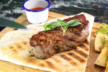 Orta pişmiş biftek, ahşap bir tahtanın üzerinde sos ve baharatlarla dilimlenmiş. Lezzetli biftek. Sebze yastığında az pişmiş biftek. Tahta tabakta biftek..