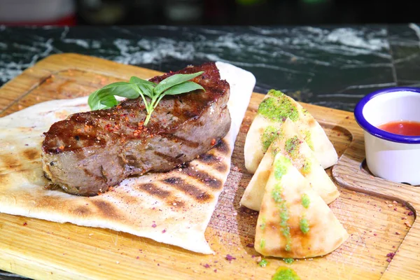 Orta pişmiş biftek, ahşap bir tahtanın üzerinde sos ve baharatlarla dilimlenmiş. Lezzetli biftek. Sebze yastığında az pişmiş biftek. Tahta tabakta biftek..