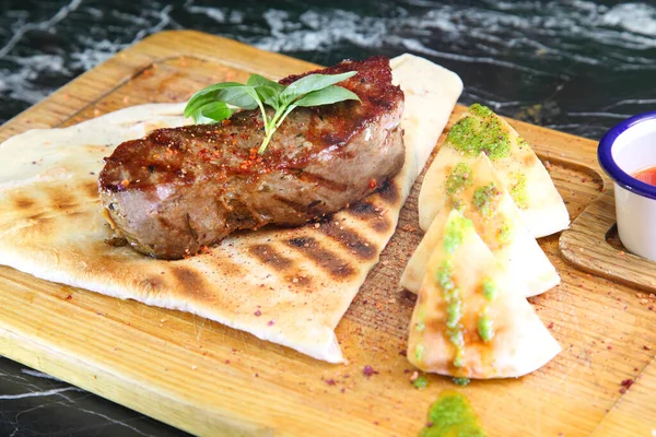 Orta pişmiş biftek, ahşap bir tahtanın üzerinde sos ve baharatlarla dilimlenmiş. Lezzetli biftek. Sebze yastığında az pişmiş biftek. Tahta tabakta biftek..