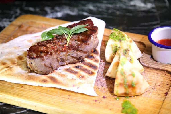 Medium-roasted steak cut into pieces on a wooden board with sauce and seasonings. Delicious steak. Beef steak medium rare on vegetable cushion. Beef steak on wooden plate.