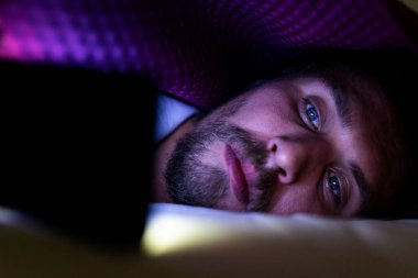 Sakallı genç adam battaniyesinin altında yatakta yatıyor. Yapamaz.