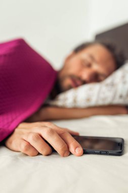 Cep telefonunu tutarken uyuyan genç ve yakışıklı bir adam. Başla.