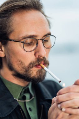 Genç yakışıklı adam sigara yakıyor.