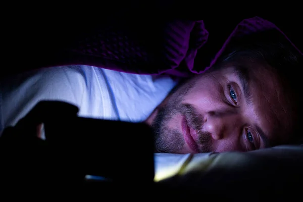 Bearded young man is lying in bed under his blanket. He cannot s Stock Image