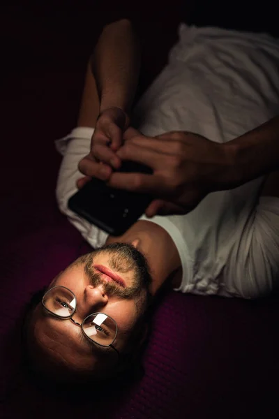 Bearded young man is lying in his bed at night while watching so Stock Picture