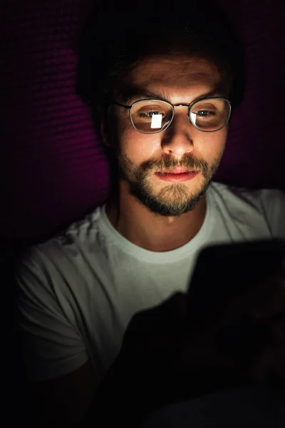 Bearded young man is lying in his bed at night while watching so Stock Picture