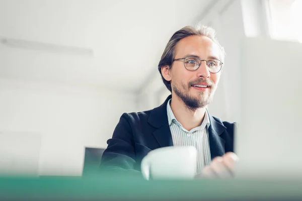 Handsome focused and smiling young man sitting by the desk worki Stock Photo