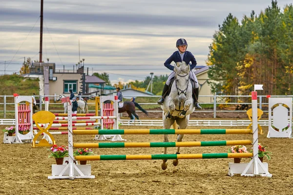 A young woman jockey on a horse performs a jump across the barrier. Competitions in equestrian sport.