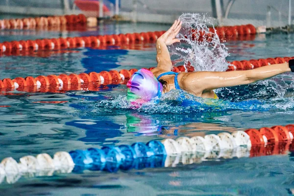 Female athlete swims with a butterfly style. Splashes of water scatter in different directions.