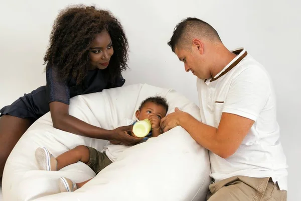 Young family. Parents feeding a infant child with milk. Wife looks tenderly at husband. Multi ethnic family.