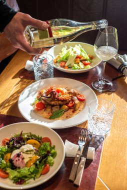 Tanınmayan garson, restoranda servis edilen yemeğin olduğu masaya şarap koyuyor.