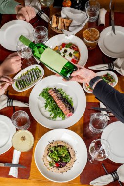 Garson şarap koyarken, bir restorandaki sette yemek yiyen tanınmamış bir arkadaş grubu. Üst görünüm