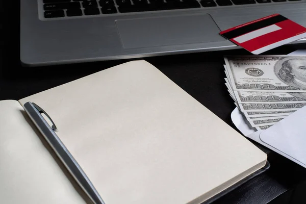 En öppen anteckningsbok med kreditkort, penna, dollar och laptop — Stockfoto