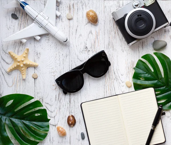 Flatlay traveler accessories on white wooden background. Monstera leaf, notebook, camera, sunglasses and plane. Top view travel or vacation concept. Summer background.