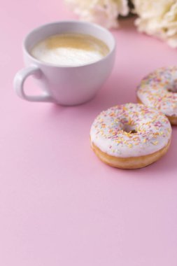 Pembe bir arka plan üzerinde iki çörek ile sıcak kapuçino Kupa.