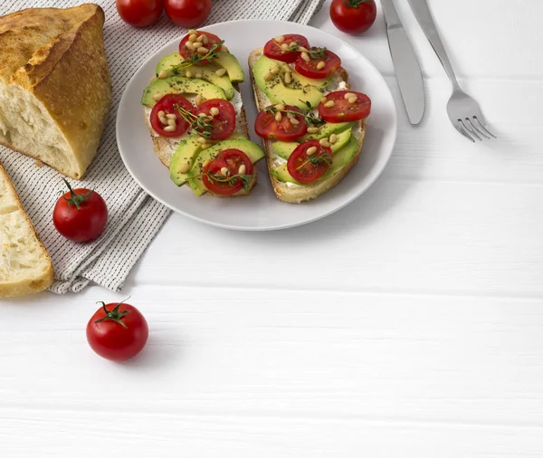 Avokado, domates, taze kekik gibi farklı sebzelerle hazırlanan iki sandviç veya tapas çam fıstığı ile parıldıyor.