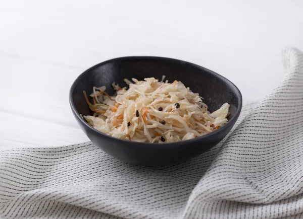 Fermented cabbage. Traditional russian appetizer sauerkraut with carrot in craft plate on white wooden table.