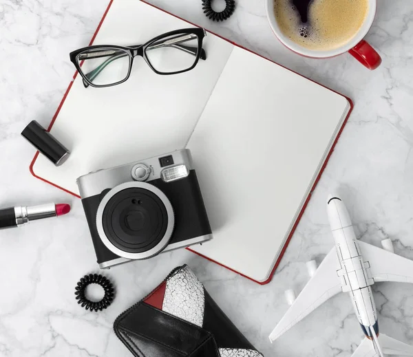 Planner, glasses, cup of coffee, camera, ear rings, hair tie, comb and lipstick at stylish marble table