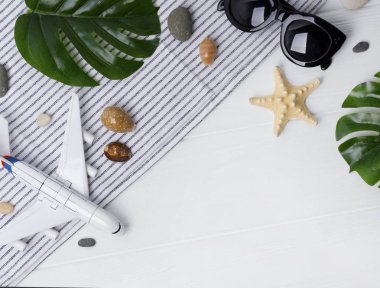 Seyahat kavramı nın zamanı. Uçak, güneş gözlüğü, monstera yaprakları, uçak, beyaz ahşap masa üzerinde yıldız balık ve havlu. 
