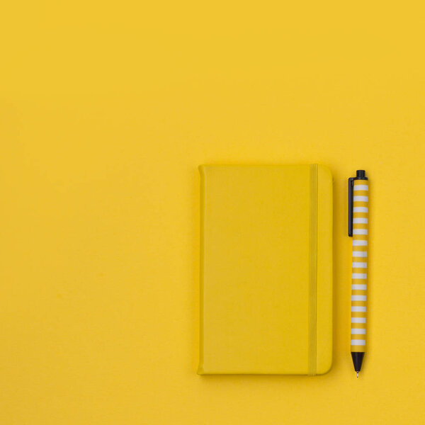 Flat lay of woman desk with notepad and pen on yellow paper back