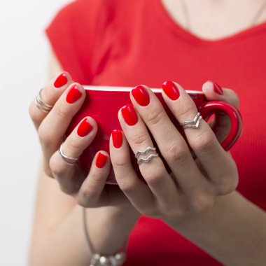 Güzel manikürlü bir kadının elleri kırmızı bir bardak cof tutuyor.