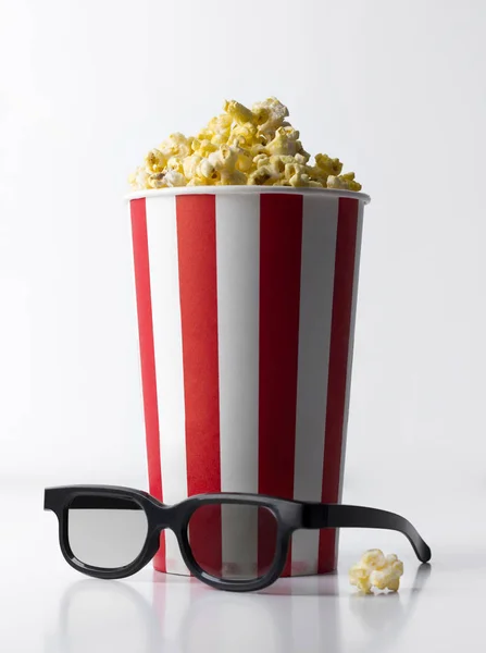 Popcorn dans un seau rouge rayé avec des verres 3D à la table blanche . — Photo