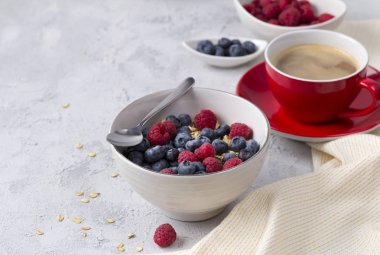 Kahve, beton arka plan üzerinde yaban mersini ve ahududu ile yulaf gevreği kase.