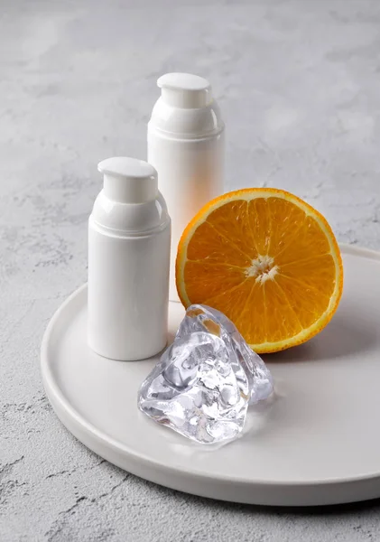 Duas garrafas de creme cosmético com laranja e gelo no concre cinza — Fotografia de Stock