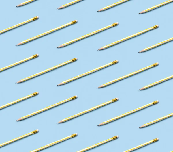 Pattern composition of yellow striped pencils on pastel blue background.